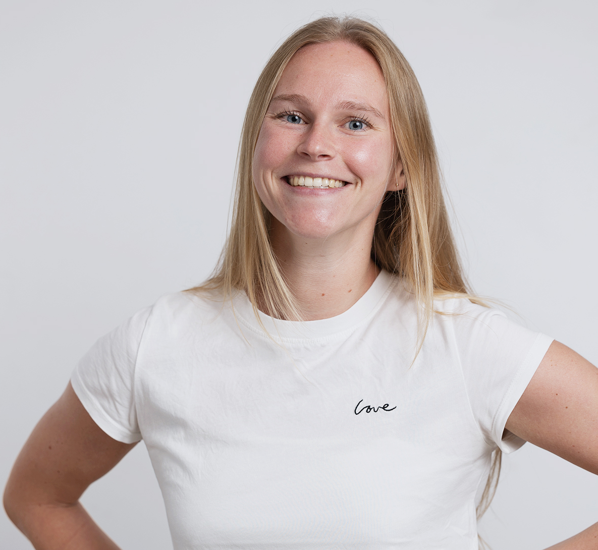 image of woman in powerpose wearing white t-shirt with long blond hair and blue eyes, smiling.